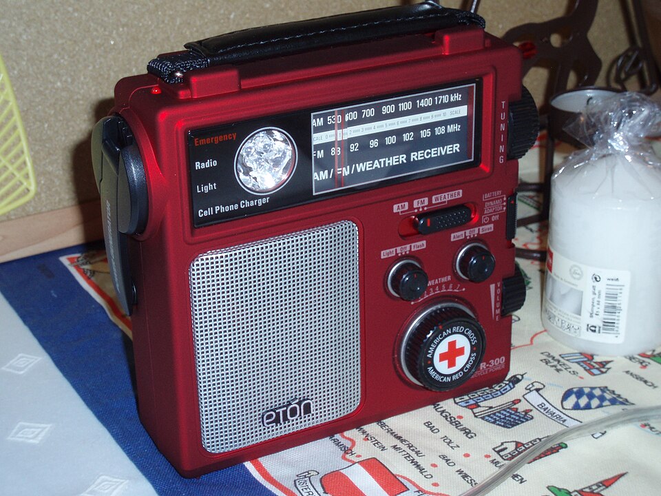 A red Eton emergency radio with a tuning dial, speaker grille and hand crank, for storm prep in Iowa City, IA